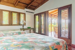 A room with two beds, a table with a bowl, and a view through a door.