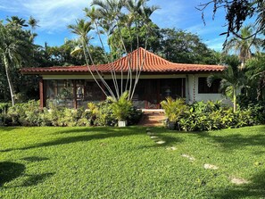 A house with a tiled roof, surrounded by a well-maintained lawn and various plants. - Golf Villa 70 - Casa de Campo - Lake and Golf View- Maid Cook Wifi - Near Beach (La Romana)