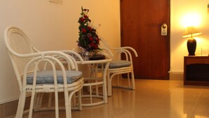 A room with three white wicker chairs with blue cushions, a small table, and a floral arrangement. - Aristocrat Inn (Dhaka)
