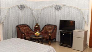 A hotel room with a bed, two armchairs, a small table with a fruit basket, a television, and a refrigerator. - Aristocrat Inn (Dhaka)