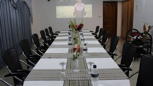Una sala conferenze con un lungo tavolo, sedie, uno schermo per proiettore e un centrotavola floreale.