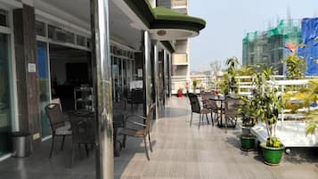 A rooftop terrace with outdoor seating, potted plants, and a view of a construction site in the background.