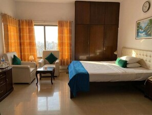 Habitación de hotel con cama, dos sillas, una mesita, armario y ventana con cortinas.