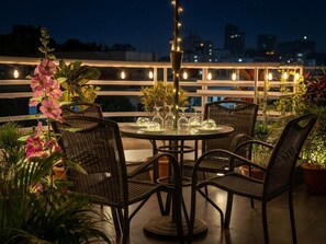 An outdoor dining area with a round table, wicker chairs, and string lights. - Aristocrat Inn (Dhaka)