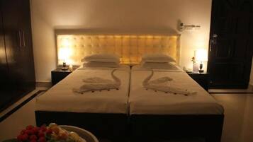 A hotel room with two beds, a headboard, bedside tables, and a small table with fruit and flowers.