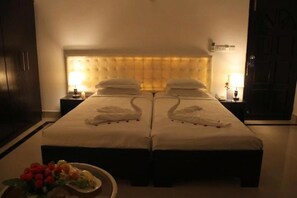 Habitación de hotel con dos camas, cabeceras, mesitas de noche y una pequeña mesa con frutas y flores.