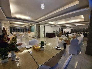 Un comedor de hotel con mesas dispuestas para los huéspedes, una recepción y vistas de la habitación contigua.