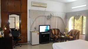 Una camera d'albergo con un letto, una scrivania con un computer, una televisione, due poltrone e un tavolino con un vaso di fiori.