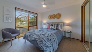 A bedroom with a large bed, a chair, a nightstand, and a window with a view of trees. - Florida Trees - Wifi Incl (INVERLOCH)