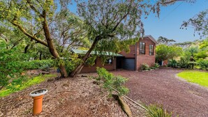 A rustic house with a gravel driveway, surrounded by lush greenery and trees. - Florida Trees - Wifi Incl (INVERLOCH)