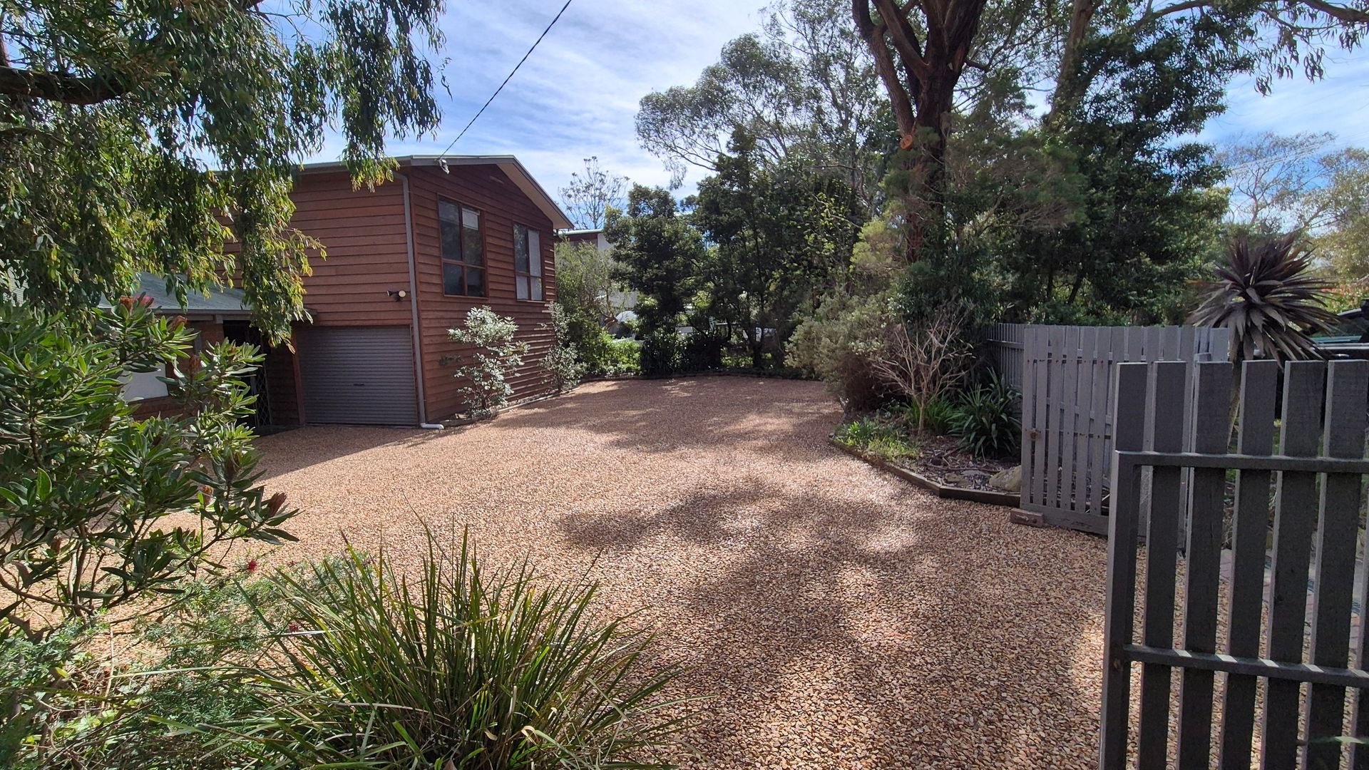 A residential property with a gravel driveway, wooden fence, and a garage.