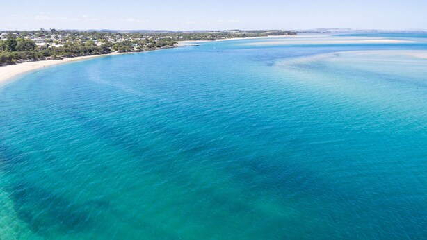 A coastal area with clear turquoise waters, a sandy beach, and a residential area with houses. - Pescarina (INVERLOCH)