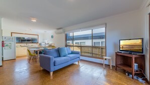 A compact living space with a kitchenette, a sofa, a TV, and a large window offering a view of the outside. - Pescarina (INVERLOCH)