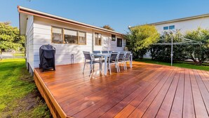 A wooden deck with a barbecue grill, outdoor table and chairs, and a view of a white building with windows. - Pescarina (INVERLOCH)