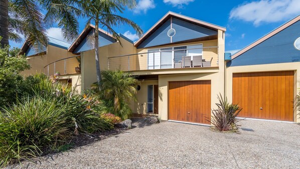 A two-story house with a driveway, a garage, and a well-maintained garden with tropical plants.