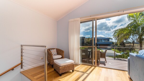A modern room with a large sliding glass door leading to an outdoor area, a wicker chair, a small table, and a metal railing. - The Sails 8 - Linen Included (INVERLOCH)