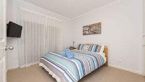 A bedroom with a bed, a television mounted on the wall, and a painting above the bed. - The Sails 8 - Linen Included (INVERLOCH)