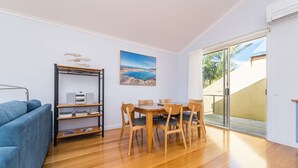A modern living room with a wooden dining table and chairs, a blue sofa, and a bookshelf with decorative fish. - The Sails 8 - Linen Included (INVERLOCH)