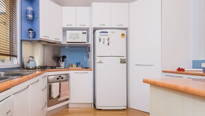 A compact kitchen with white cabinets, a microwave, a refrigerator, a stove, and a kettle. - The Sails 8 - Linen Included (INVERLOCH)