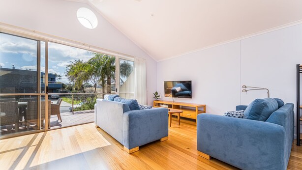 A modern living room with large windows, a flat-screen TV, and two blue sofas. - The Sails 8 - Linen Included (INVERLOCH)
