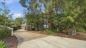 A residential property with a driveway leading to a house, surrounded by mature trees and shrubs.