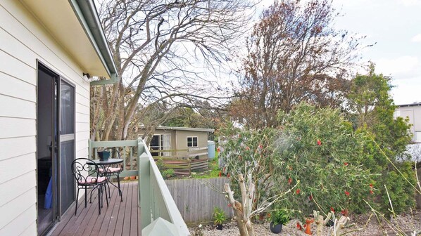 A deck with outdoor furniture, a wooden fence, and a garden with various plants and a tree.