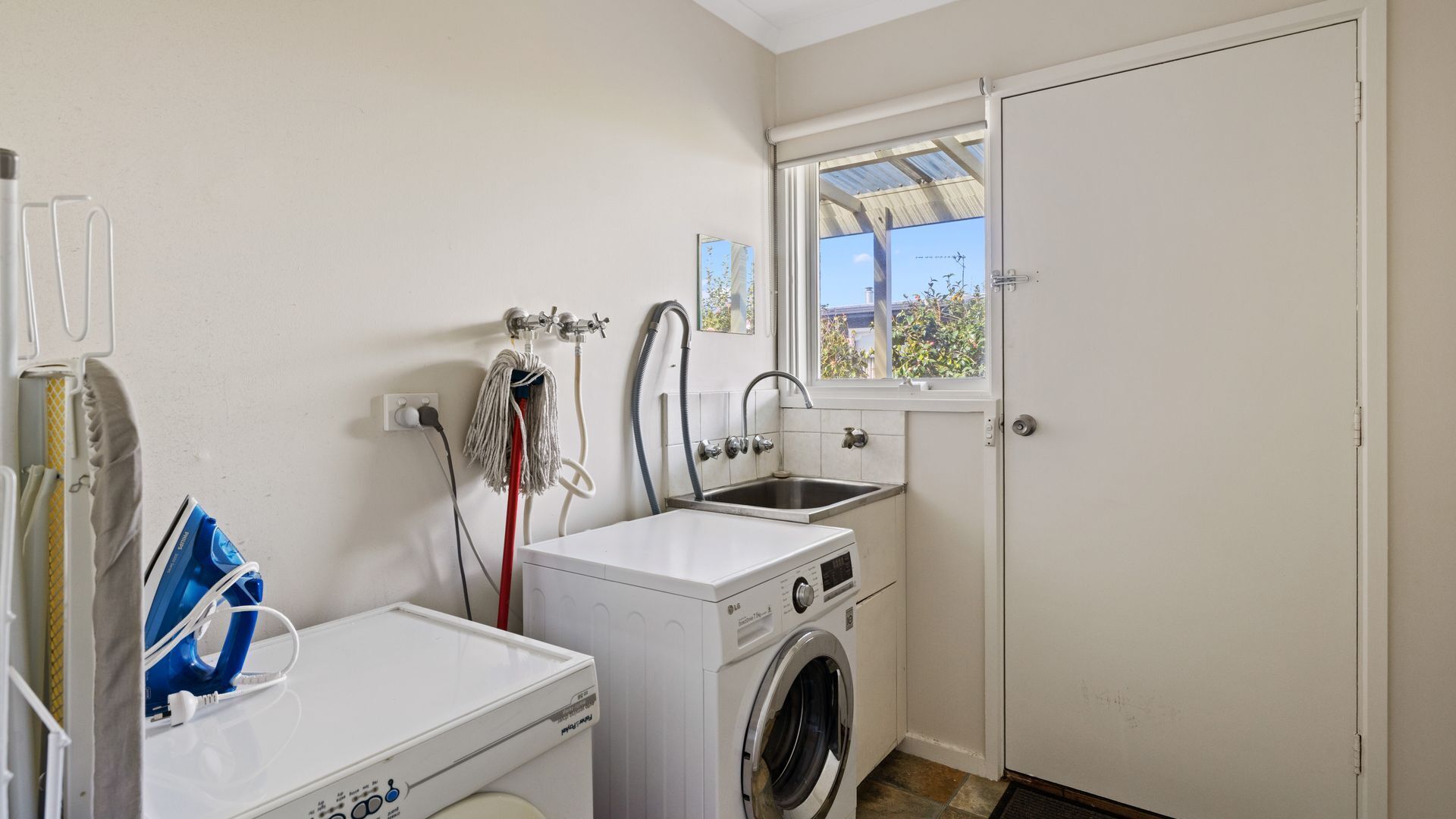 Une petite buanderie équipée d’un lave-linge, d’un sèche-linge, d’un évier et d’une fenêtre.