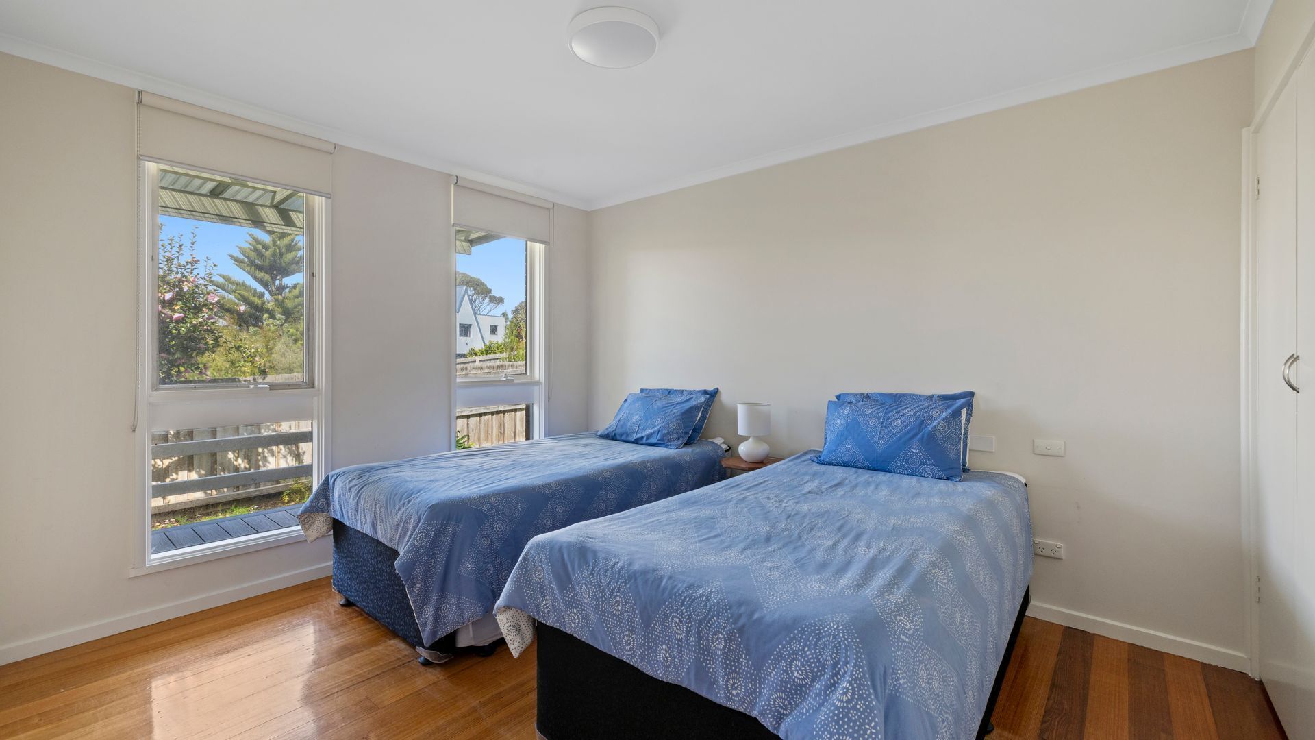 A bedroom with two beds, large windows, and a view of a garden.