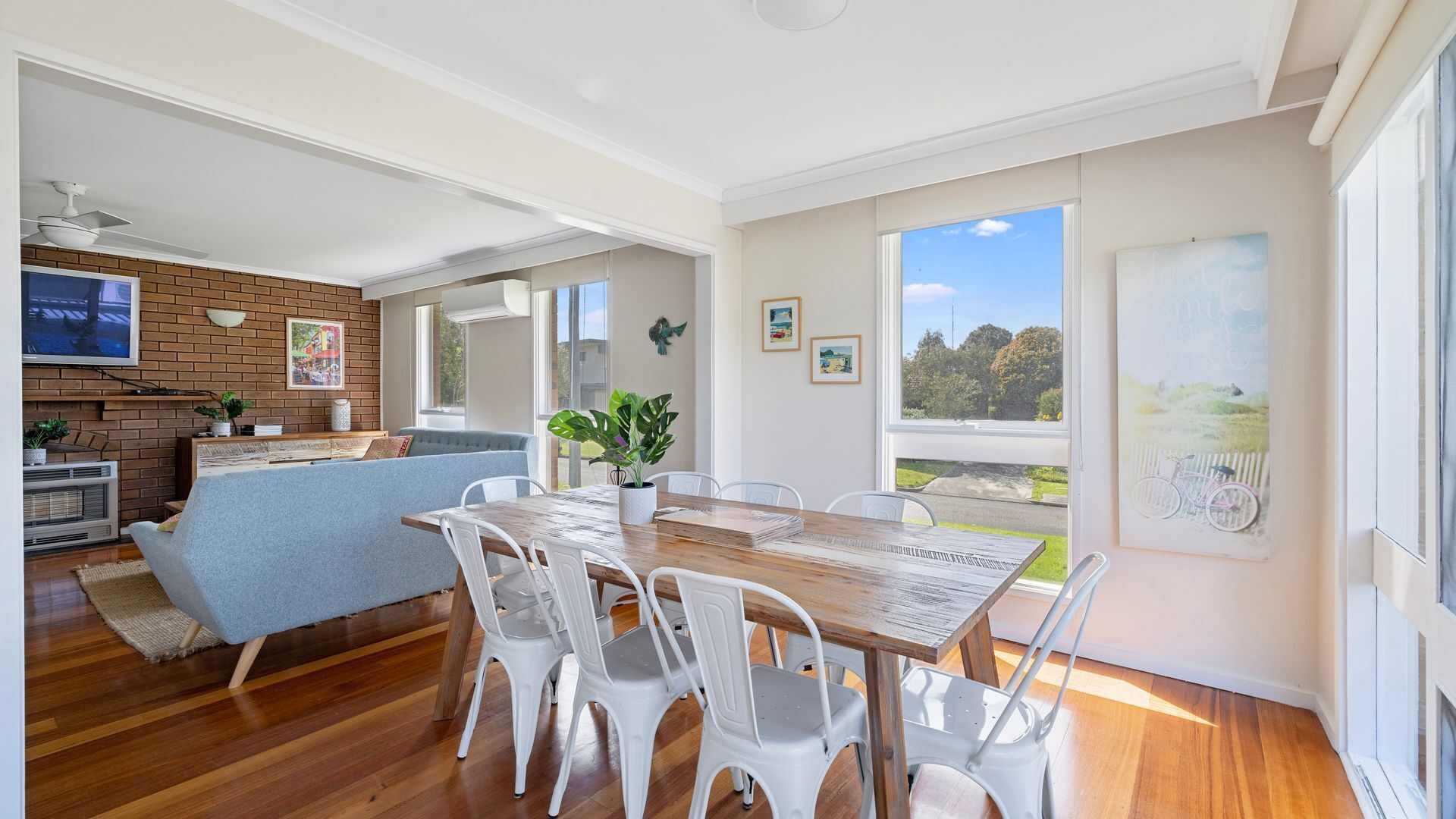A modern kitchen with a brick backsplash, a dining area with a wooden table and white chairs, and a large window offering a view of the outdoors.