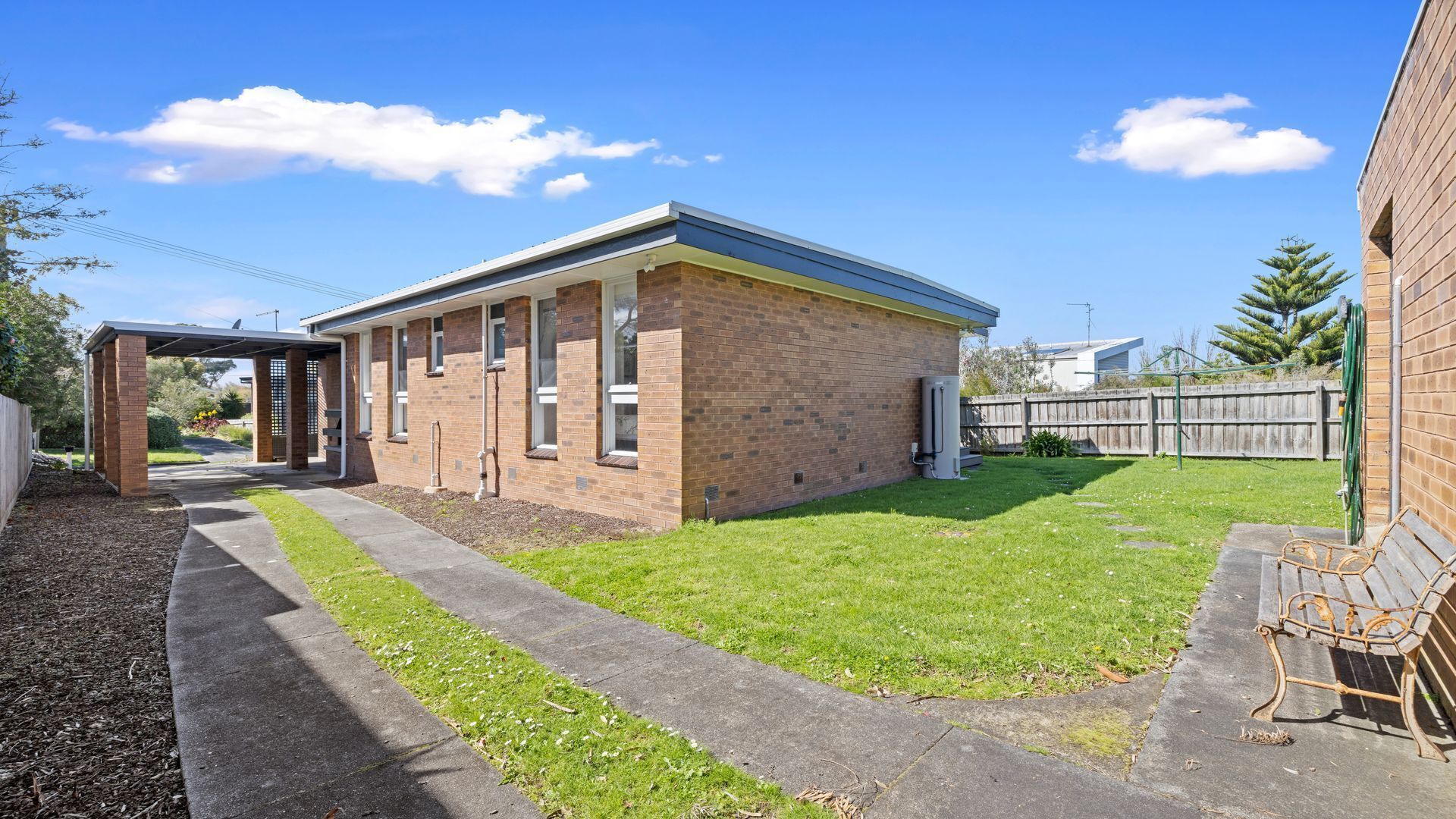 A single-story brick building with a covered patio area, a grassy yard, and a wooden fence.