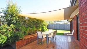 A patio with a table and chairs, a wooden deck, and a brick wall. - Plovers Rest Inverloch (INVERLOCH)