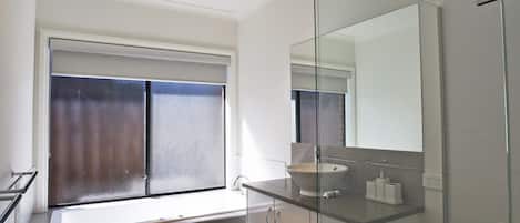 A modern bathroom with a glass shower enclosure, a sink with a mirror, and a window with frosted glass.