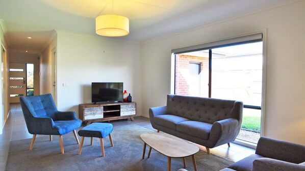 A modern living room with a grey sofa, blue armchairs, a coffee table, and a TV on a wooden stand.