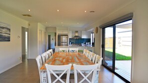 A modern kitchen with stainless steel appliances, a dining area with a patterned tablecloth, and a sliding glass door leading to a backyard. - Plovers Rest Inverloch (INVERLOCH)