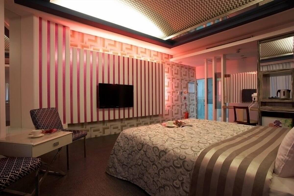 Ein modernes Hotelzimmer mit einem großen Bett, einem Schreibtisch, einem Sessel und einem Fernseher.