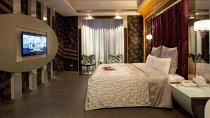 A hotel room with a large bed, a television mounted on the wall, a bedside table with a lamp, and a large mirror. - Love Star Motel (Taoyuan City)