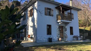 Ein zweistöckiges Haus mit Balkon, Steinwänden und einem kleinen Garten mit Gartenmöbeln.