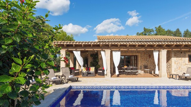 A poolside area with a tiled roof, outdoor seating, and a clear blue pool.