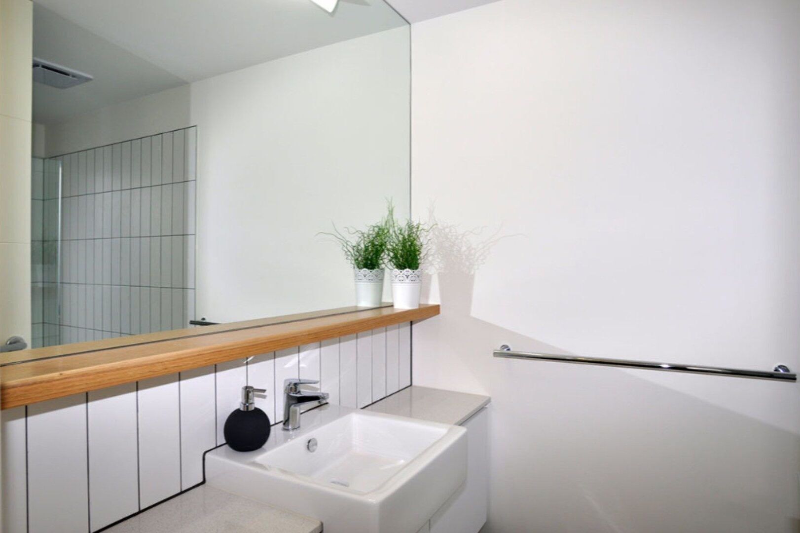 Une salle de bain moderne avec un lavabo blanc, un plan de toilette en bois, un miroir et un porte-serviettes.