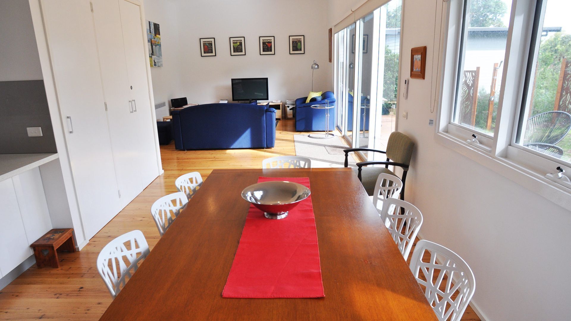 A dining area with a wooden table, white chairs, a red placemat, and a silver bowl.