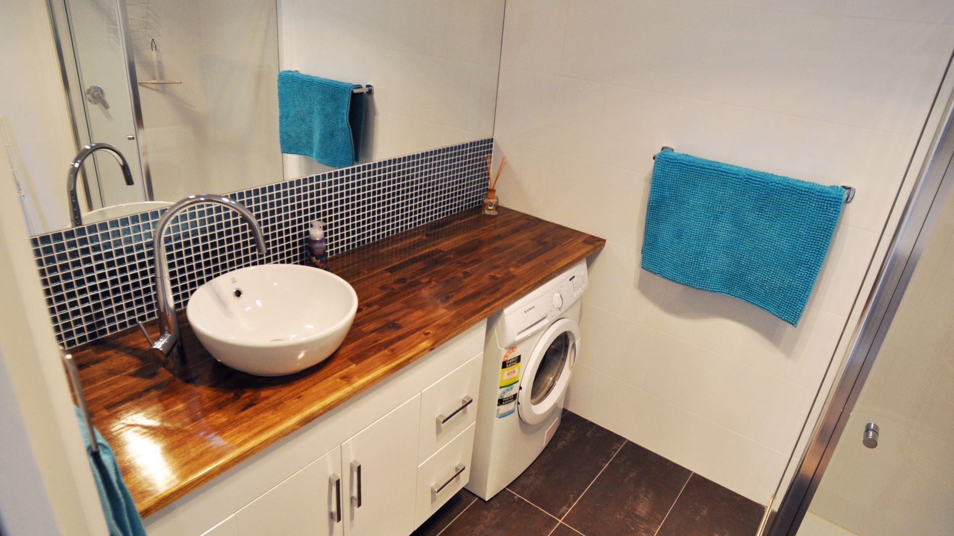 Une salle de bain avec un meuble-lavabo en bois, un lavabo blanc, un lave-linge et des serviettes bleues.