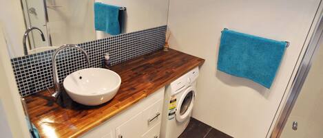 Une salle de bain avec un meuble-lavabo en bois, un lavabo blanc, un lave-linge et des serviettes bleues.