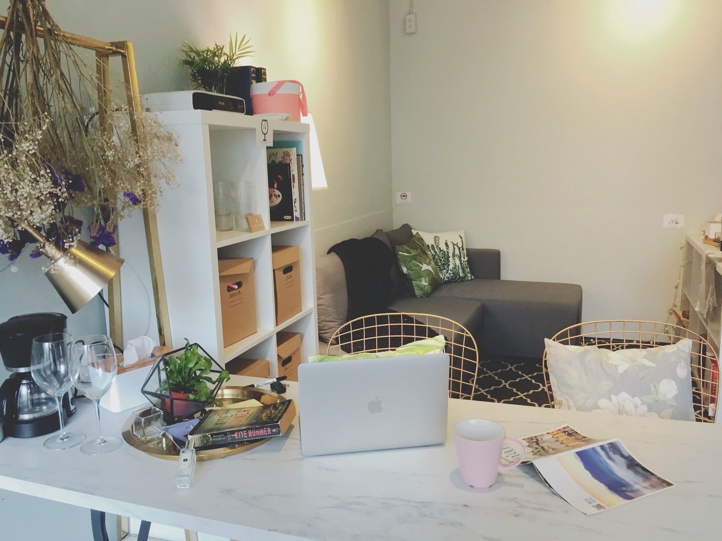 A modern living room with a white sofa, a coffee table with a laptop, a bookshelf, and a decorative plant.