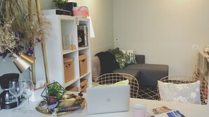 A modern living room with a white sofa, a coffee table with a laptop, a bookshelf, and a decorative plant. - We2 AnPing Hostel (Tainan)