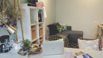 A modern living room with a white sofa, a coffee table with a laptop, a bookshelf, and a decorative plant.