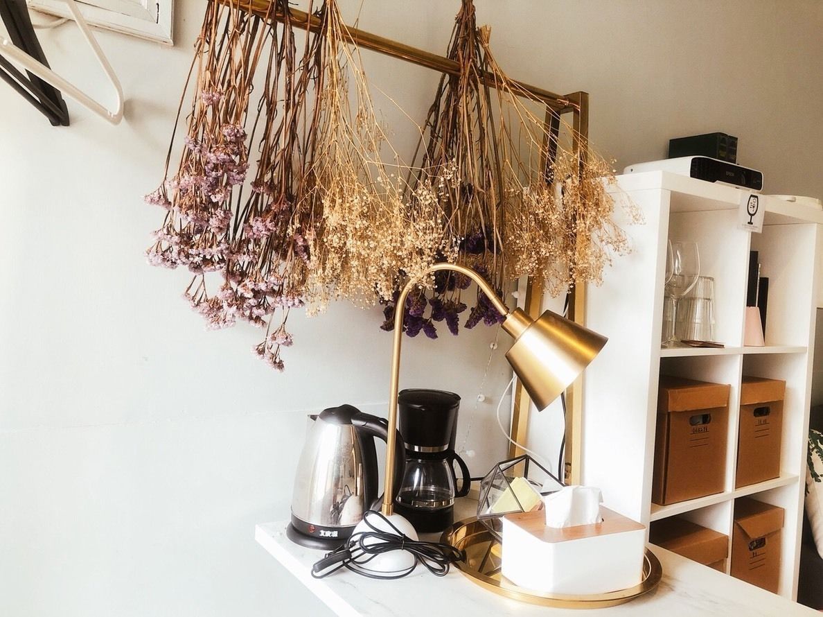 A desk with a coffee maker, a lamp, and a vase with dried flowers.