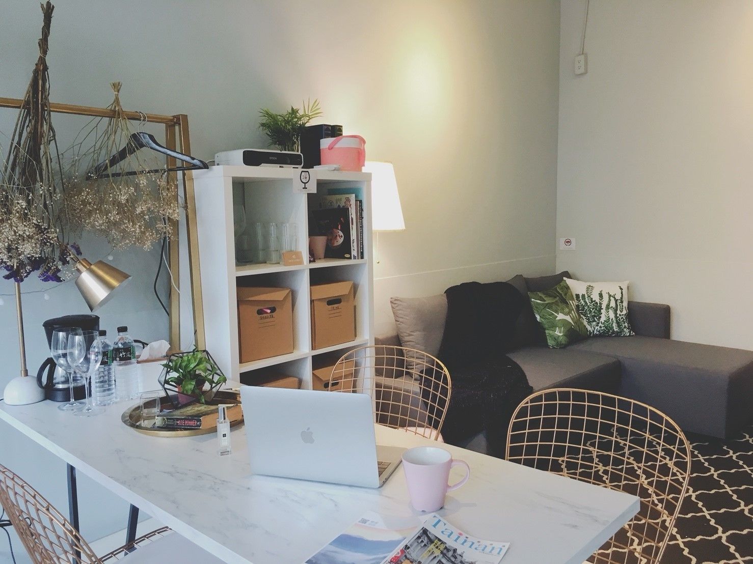 A modern living space with a white sofa, a coffee table with a laptop, a bookshelf, and a hanging plant.