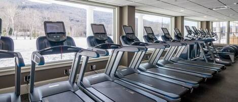 A gym with treadmills and stationary bikes, large windows, and a view of mountains.
