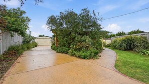 A residential driveway leading to a garage, surrounded by lush greenery and a wooden fence.