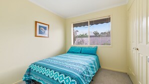 Um quarto com uma cama, janela com persianas, porta e um quadro na parede.
